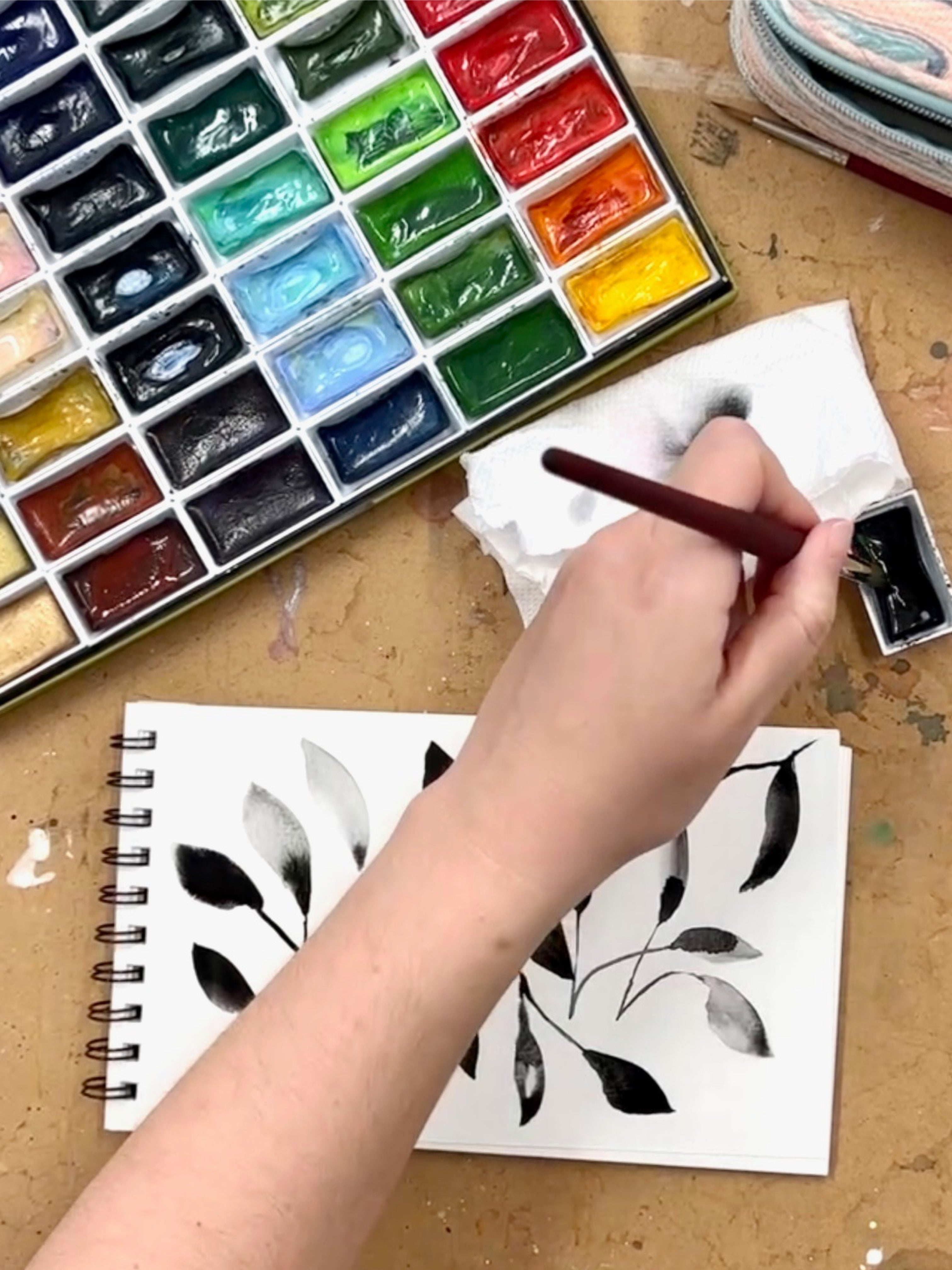 A print of the ghost petal flowers on a paper pad next to a watercolor paint palette