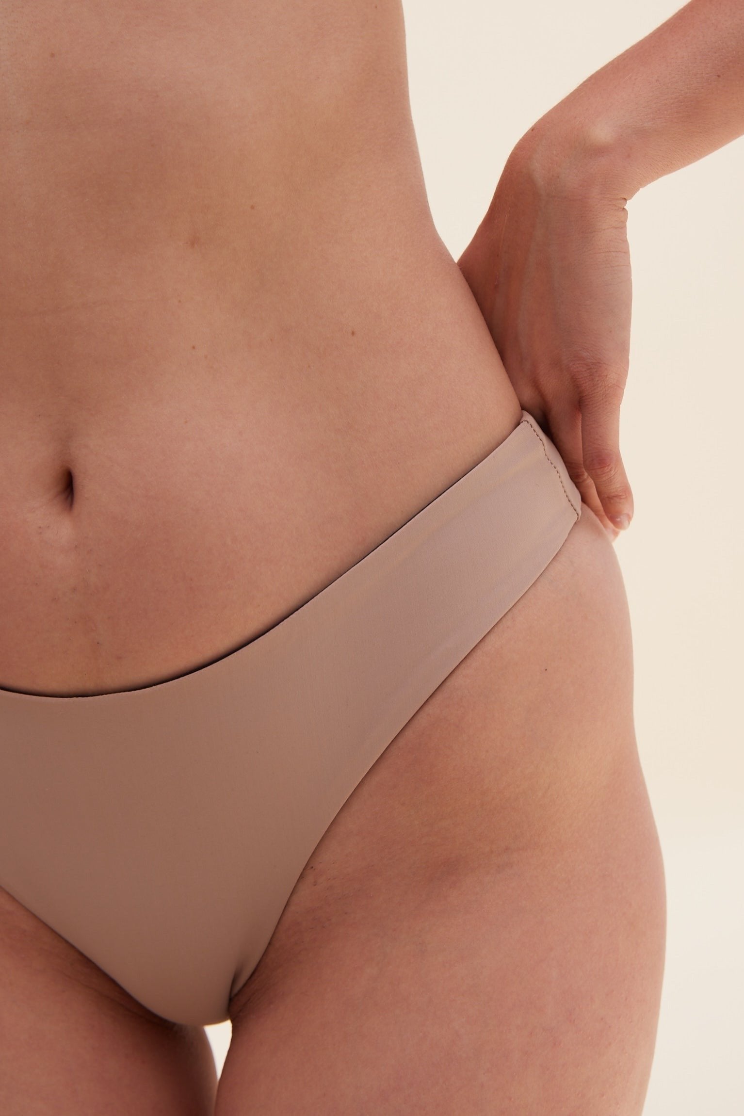 Close-up front view of model wearing Reversible Koloa Mid Rise Bottom in dune color with tan style